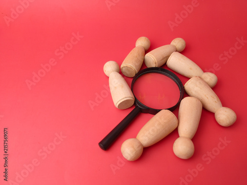 Foto Seven wooden peg figures lie scattered in a circle around a black magnifying gla
