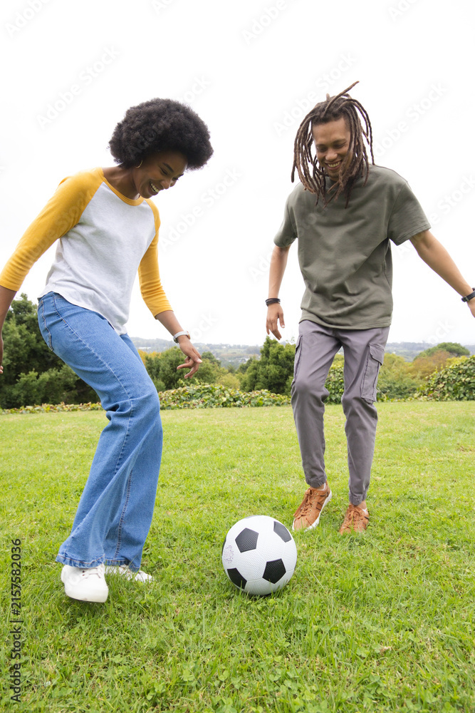 Fototapeta premium African American friends kicking black-white soccer ball on grassy slope showing bracelets
