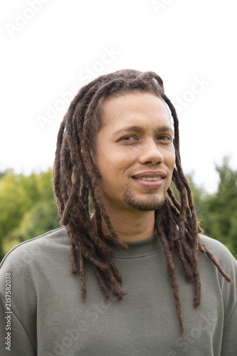 African American man standing and smiling outdoors in park wearing olive crewneck sweatshirt