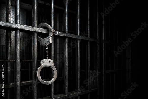 Metal Handcuffs Hanging on Dark Prison Cell Bars Representing Crime Justice Imprisonment and Loss of Freedom
