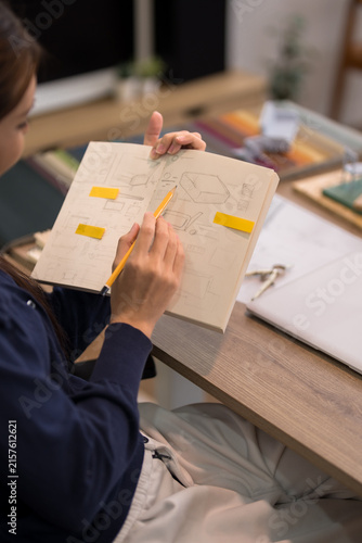 Young Asian furniture designer sketching product blueprint with yellow sticky notes in creative studio workspace