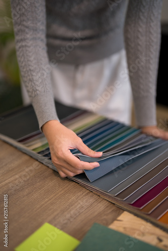Asian furniture designer selecting gray fabric swatch from colorful material sample palette in modern studio