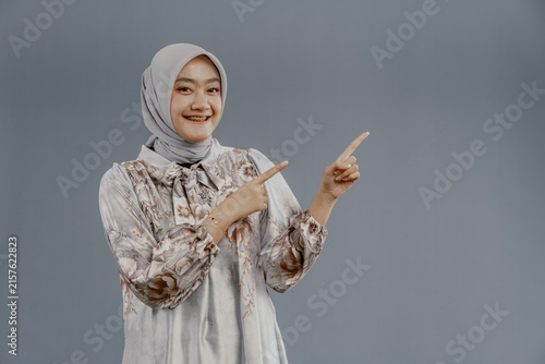 Portrait happy young asian muslim female standing on isolated pointing finger hands to blank space for text advertisement. Beautiful Attractive Muslim woman wearing hijab fashion costume.