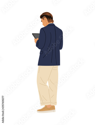 Man stands, back turned, holding tablet. Dressed in navy blazer and beige trousers. Neutral stance suggests focus or thoughtfulness. Ideal for business, tech, or modern professional scenes