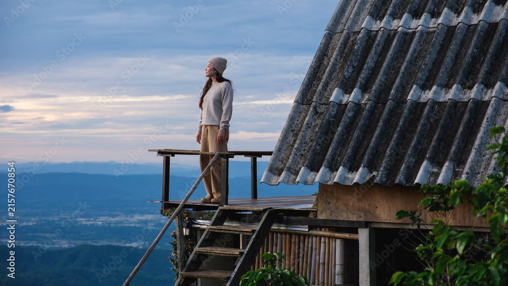 Fototapeta premium A woman standing on wooden balcony, looking at mountain views on cloudy morning