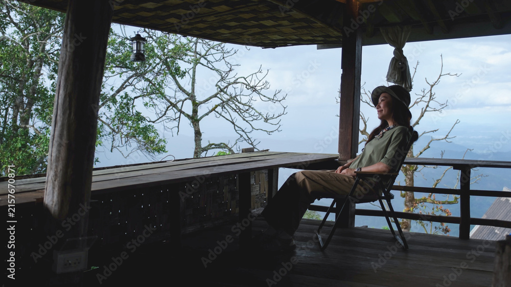 Fototapeta premium Portrait of a woman sitting on wooden balcony and looking at mountain views