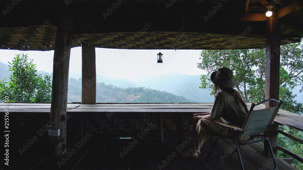 Fototapeta premium Rear view of a woman sitting on wooden balcony and looking at mountain views