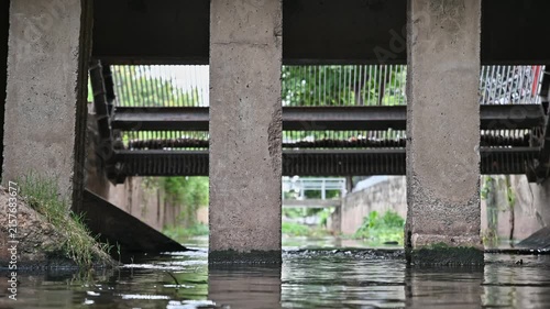 Concrete drainage channel with flowing water beneath an urban infrastructure structure