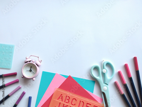 Back to school supplies flat lay with colorful paper, pencils, alarm clock, and alphabet stencil on white background