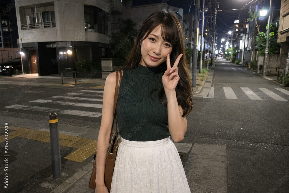 Fototapeta premium 緑トップスと白スカートで夜道に立つ女性