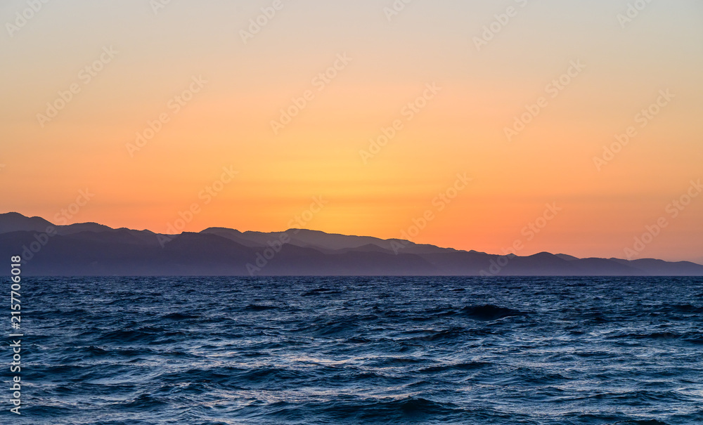 Fototapeta premium Majestic sunset over tranquil ocean waves and distant mountains near the shore