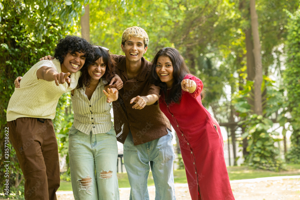 Fototapeta premium Group of diverse indian asian Gen z young adult friends laughing and embracing each other outdoors, sharing a happy moment and representing youth, unity, and friendship in a summer park. .