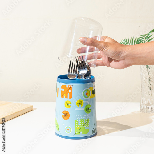 фотографія Person holds a plastic cover over a utensil holder.