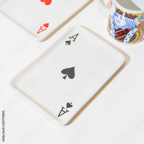 Konstfotografi Saucer with playing card print rests on table.