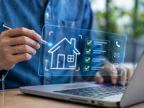 Real estate technology concept with a hand interacting with a holographic house display and laptop