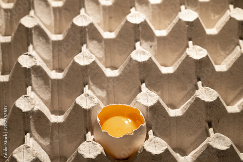 cardboard carton container with one broken egg showing yolk.