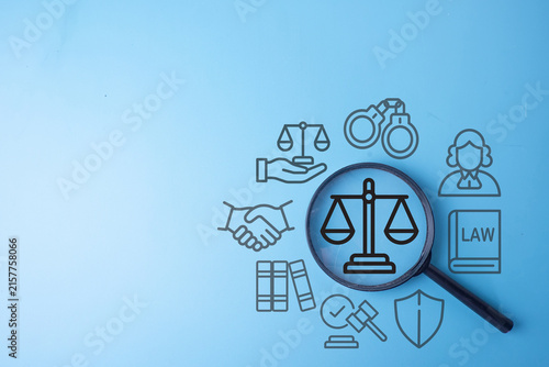 Magnifying glass focusing on a justice scale icon surrounded by judge, law book, and handshake graphics on a blue background. Concept of legal services, justice system, and law enforcement.