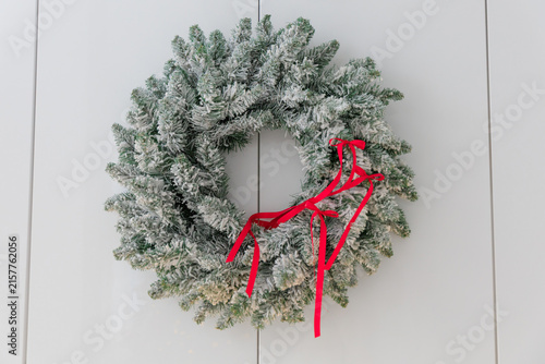 Obraz na płótnie Holiday wreath hangs on a white wall with red ribbon detail showing winter decor