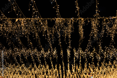 Fotografie Bright lights hang above a nighttime scene in a festive setting with decorations