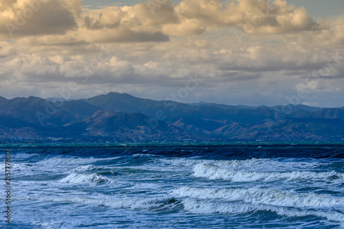 Photography Waves crashing against the shore at sunset with mountains in the distance and dr