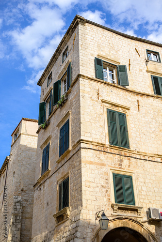 A historic multi-story stone building in an old European town with dark green shutters