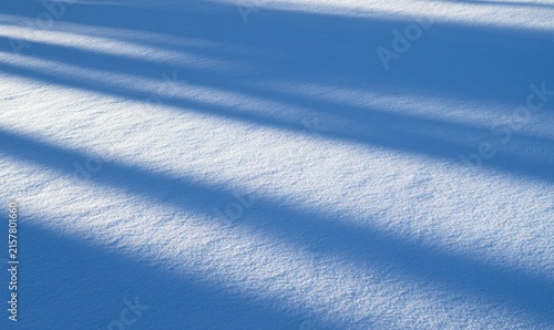 Diagonal shadows cast across a textured expanse of pristine white snow