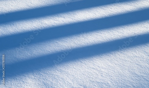 Diagonal shadow stripes cast across a textured, bright white snowfield