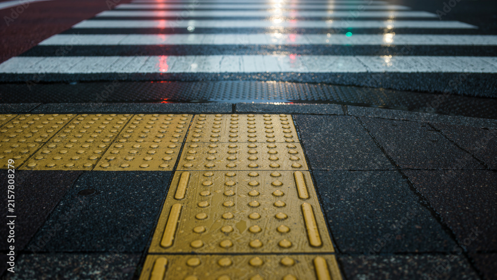 Fototapeta premium Yellow tactile paving tiles leading to a wet pedestrian crossing