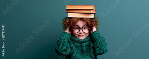 cheerful young Black child with curly afro hair, , balancing two hardcover books on top of her head	
