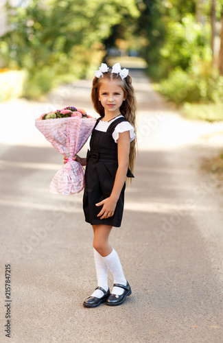 Fotografía Charming little schoolgirl holding flower bouquet on her way to school on autumn