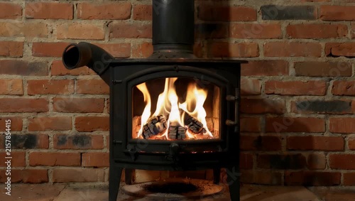 A classic black wood-burning stove with energetic yellow and orange flames dancing behind glass against a rustic brick wall conveying warmth and cozy home comfort