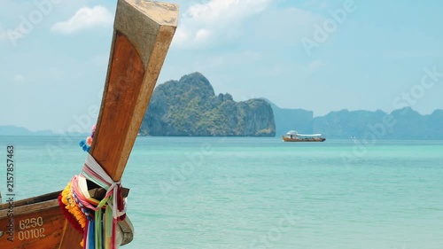 Longtail boat prow decorated with colorful sashes floating near turquoise water, limestone island background in Andaman Sea, tropical Thailand travel destination advertisement