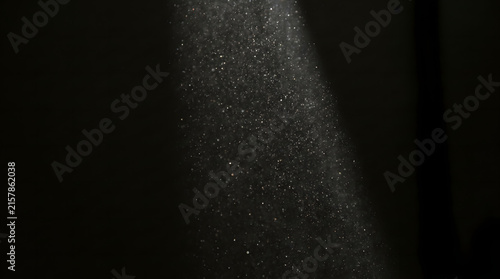 Bright sunbeam illuminating floating dust particles against a dark background for mystery