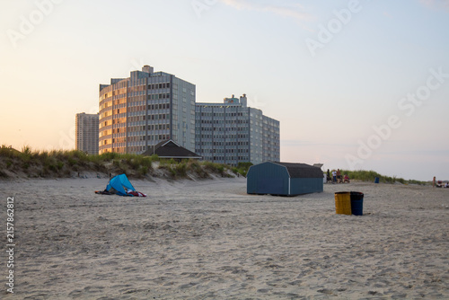 Atlantic City, New Jersey, USA - October 5, 2024: The Ocean at 101 Boardwalk condominium buildings rising behind coastal sand dunes and a beach area at sunrise, featuring a blue sun tent and storage s