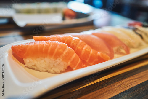 Row of salmon nigiri sushi on a white plate from an angle