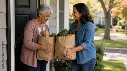 Smiling middle-aged woman delivering grocery bags to an elderly woman at her front door, exchanging fresh produce and bread in a friendly neighborhood setting
