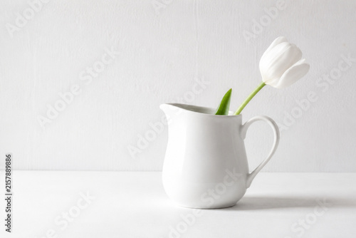 White ceramic milk pitcher with single tulip on white tabletop, minimalism and purity concept