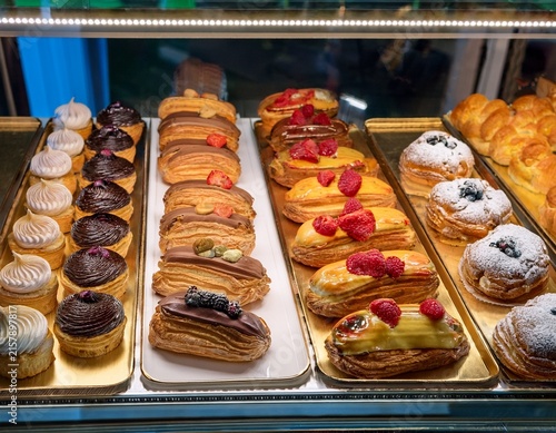 assorted french pastries displayed in a bakery case including eclairs mille feuille cream puffs and fruit tarts