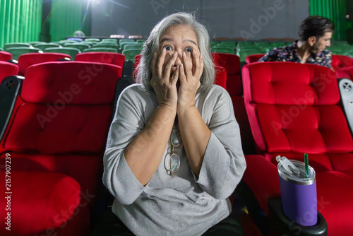 Quadro su tela Shocked senior woman covering face while watching scary movie in cinema
