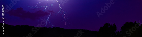 Obraz na płótnie Éclairs ramifiés illuminant un ciel d’orage violet au-dessus d’un paysage noctur