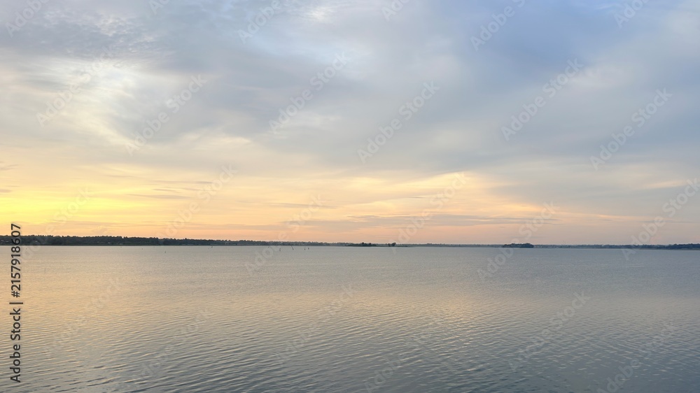 Obraz premium Serene Golden Sunset Over Calm Lake Water with Cloudy Sky Horizon