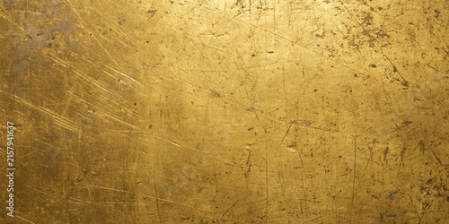 Textured brass surface with scratches and patina under warm directional lighting for background use