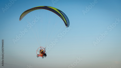 Quadro su tela Powered paraglider with a trike flies high in the clear blue sky, capturing a moment of extreme sport and extreme freedom
