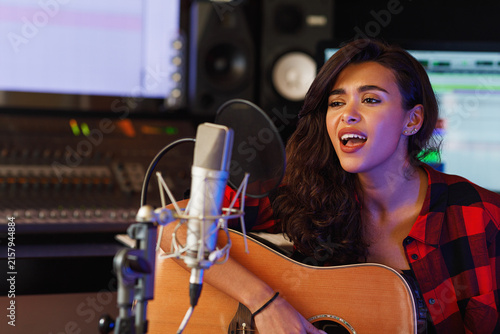 Young woman singing and playing one acoustic guitar in a recording studio