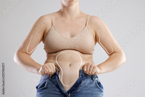 Photography Overweight woman trying to put on tight jeans against gray background, closeup
