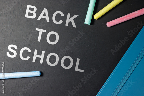 Bild auf Leinwand Top view composition of Back to School text printed on a black board with colorful chalk pieces and a blue notebook edge
