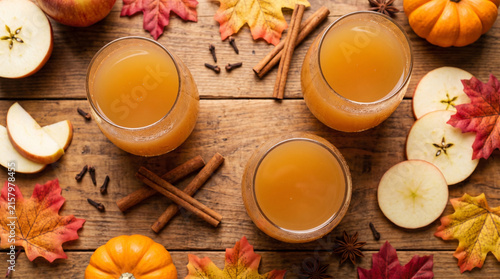 Autumn apple cider in glass with cinnamon and seasonal fruit creates warm rustic harvest scene