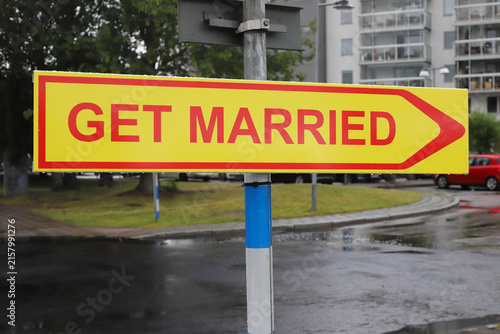 Yellow “GET MARRIED” wedding sign pointing right on residential street
