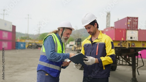 Fotografía Two logistics workers discuss a shipping manifest on a clipboard in a container yard, collaborating on supply chain management and cargo inspection, reflecting teamwork and modern workplace themes