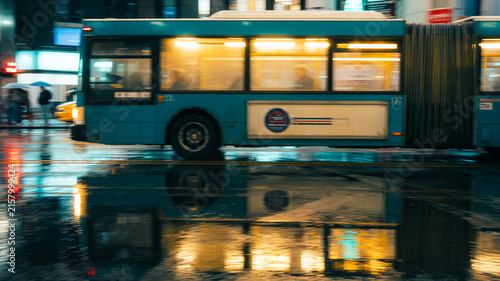 Realistic City Bus At Night With Glowing Interior, Wet Road Reflections, Street Photography Look.
